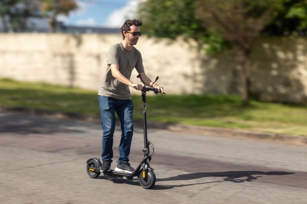 Patinete Elétrico para Adultos: tudo que você precisa saber antes de escolher o seu 2 Homem pilotando patinete elétrico para adultos em via urbana durante o dia, usando óculos escuros e demonstrando uma opção prática, confortável e sustentável para mobilidade urbana.